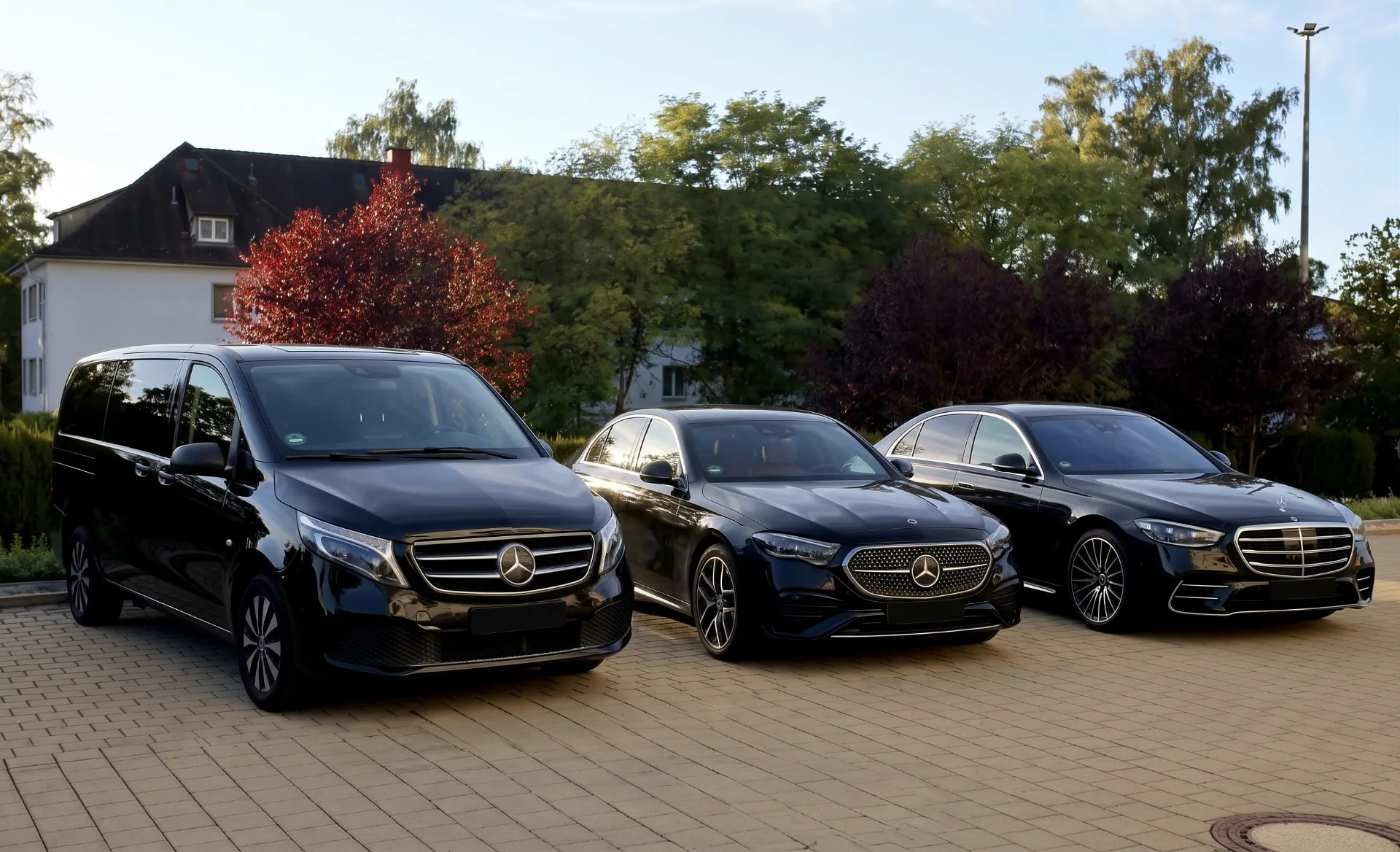Schwarze Mercedes-Benz V-Klasse, E-Klasse und S-Klasse vor einem Gebäude mit Bäumen